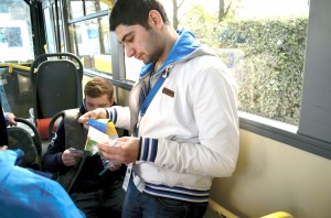 Two young Russian men read the gospel presentation that was attached to the Engage Sochi pins as they ride the bus in Sochi, Russia. Members of the Singing Men of Oklahoma and their companions each had 50 pins to trade or share with those they met on their recent trip to the XXII Winter Olympics (Photo: Bob Nigh)