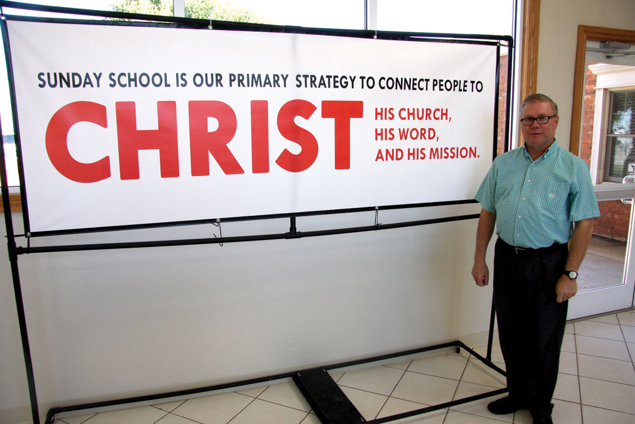 Pastor Kevin Baker of Altus, Martha Road, by a banner that reminds church members of the mission of Sunday School (Photo: Brian Hobbs)