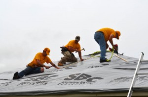 From left, Scott Cross, David Philpott and Paul Gustafson tarp the roof of a home in Bridge Creek. (Photo: Bob Nigh)